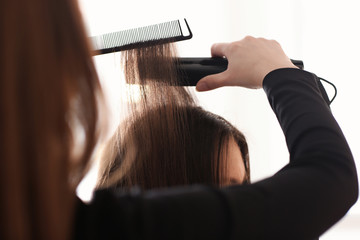Professional hairdresser straightening client's hair in salon