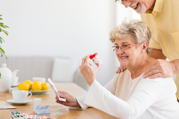 Smiling senior woman looking at container with hypertensive drugs