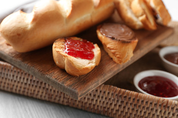 Wicker tray with delicious toasts, jam and chocolate paste on table