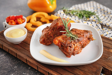 Plate with delicious grilled ribs, sauce and vegetables on wooden board