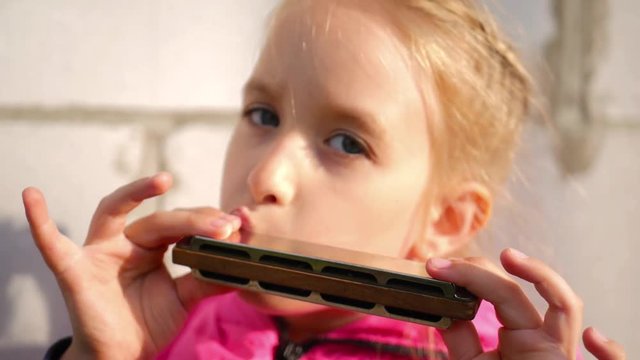 Pretty little girl playing harmonica in outdoors.