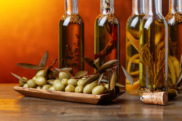Green olives and bottles of olive oil with warious spices and herbs .