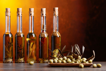 Green olives and bottles of olive oil with warious spices and herbs .