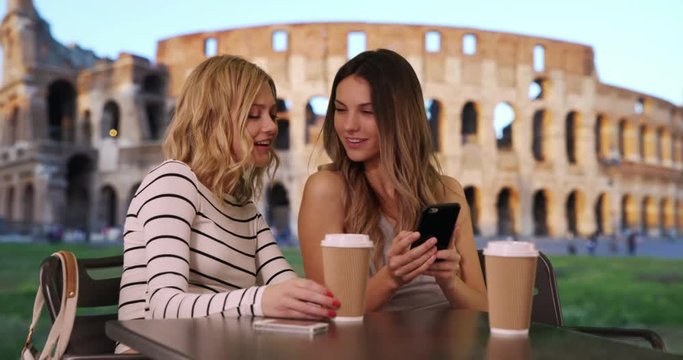 Portrait of couple of happy girlfriends sitting at table taking selfie in front Roman Colosseum, Cute white girls seated taking selfie with smart phone in Rome, Italy, 4k