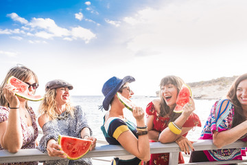 blue and red colours image of group of females friends stay together and have fun in the summer eating a watermelon. smiles and laugh enjoying a perfect sunny day of vacation