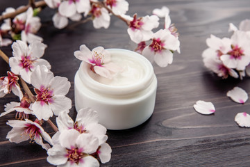 Fototapeta na wymiar Jar of cream and blooming flowers on wooden background
