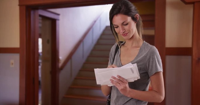 Young Caucasian woman looking through mail she received in domestic home setting, White millennial female checking stack of letters standing inside her house, 4k