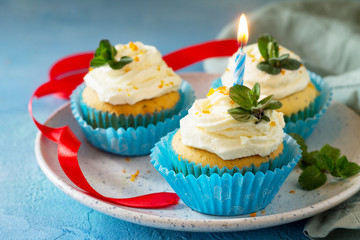 Colorful cupcake with whipped cream, poppy and orange peel on a blue a stone or slate background.