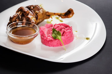 Fried chicken shin with sauce and pink potatoe puree on black background