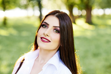 Cute young brunette girl with beautiful professional make-up on green background in park