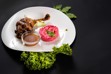 Fried chicken shin with sauce and pink potatoe puree on black background
