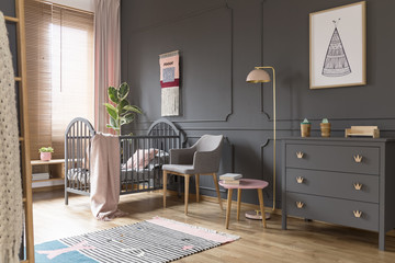 Grey cabinet next to pink lamp in simple baby's bedroom interior with blanket on bed. Real photo
