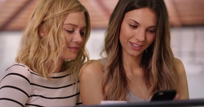 Close up of pretty brunette woman showing blonde friend smart phone indoors at home, Close view of two friends sharing smartphone inside house, 4k