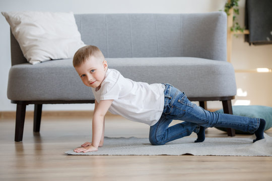 Photo of boy in white T-shirt playing on floor near sofa