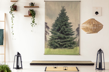 Real photo of a tatami mat between two black lanterns in oriental apartment interior with tree graphic on the white wall