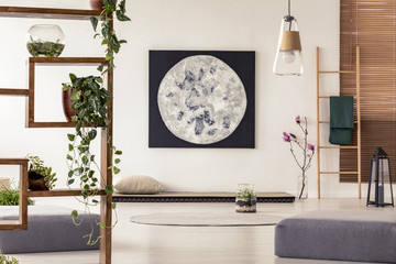 Moon painting above tatami mat bed in japanese style flat interior with ivy on wooden rack and...