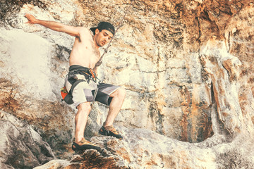 Young male climber hanging on a safety rope in the mountains. Toned
