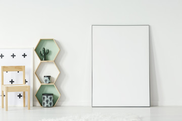 Wooden chair and hexagon shelves next to poster with mockup in kid's room interior. Real photo. Place for your graphic
