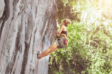 Female climber climbing a cliff with a safety rope on a sunny summer day