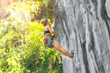 Young woman climbing a cliff with a safety rope on a sunny summer day