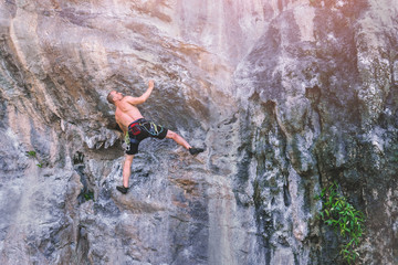 Young male mountaineer climbs on a rocky wall without insurance