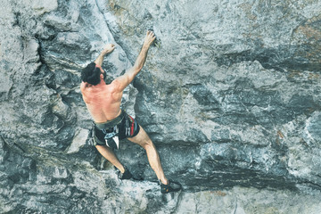 A young bearded man is climbing a rock