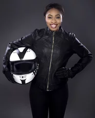 Fotobehang Black female motorcycle biker or race car driver or stuntwoman wearing leather racing suit and holding a protective helmet.  She is standing confidently in a studio © Innovated Captures