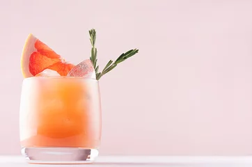 Crédence de cuisine en verre imprimé Bar Cold lemonade of fresh grapefruit juice, alcohol and ice cubes decorated slice citrus and twig rosemary on fashion pastel pink background.