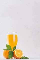 Fresh vitamin yellow summer beverage of ripe oranges with green leaves on light white wood background, vertical.