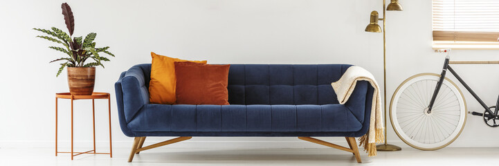 Real photo of a simple living room interior with orange cushions on a navy blue sofa standing...