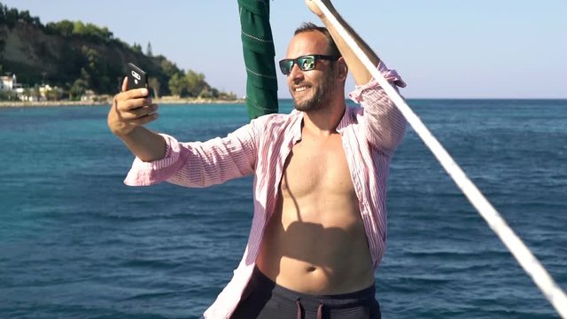 Young man taking selfie photos with cellphone while sailing boat on sea
