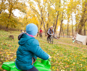 Little boy on a children's bicycle looks at adult cyclists in an autumn park. The concept of...