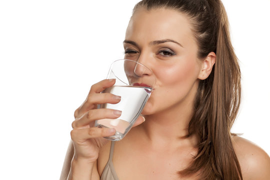 happy woman drinks water from a glass on white background and winks