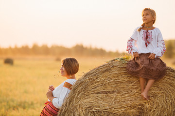 A girl and woman in embroidered clothes in the field in the background of the setting sun