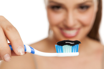 young woman holds a toothbrush with black toothpaste from an active coal to a white background