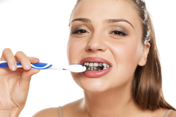 young woman brushing her teeth with black toothpaste of activated charcoal on white background