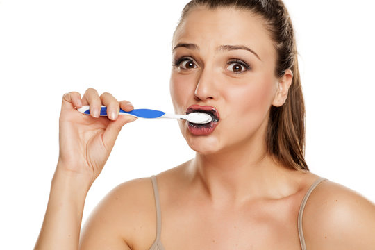 young woman brushing her teeth with black toothpaste of activated charcoal on white background