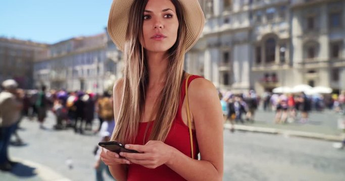 Stylish woman in red top using phone and looking around while in Rome, Italy, Caucasian hipster girl in her 20s texting on smartphone while on vacation in Rome, 4k