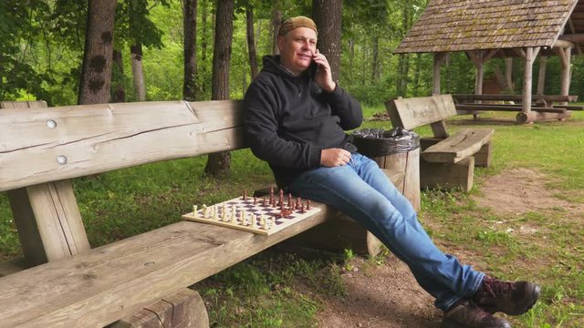 Man sitting near chessboard and talking on smartphone