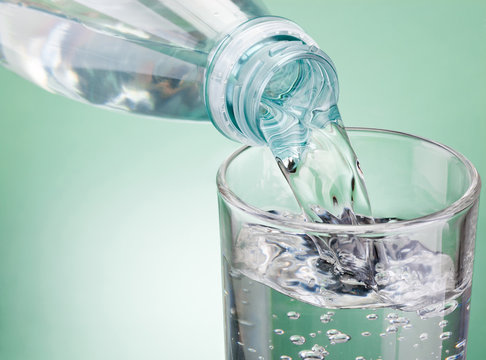 Pouring water from bottle into glass on green background