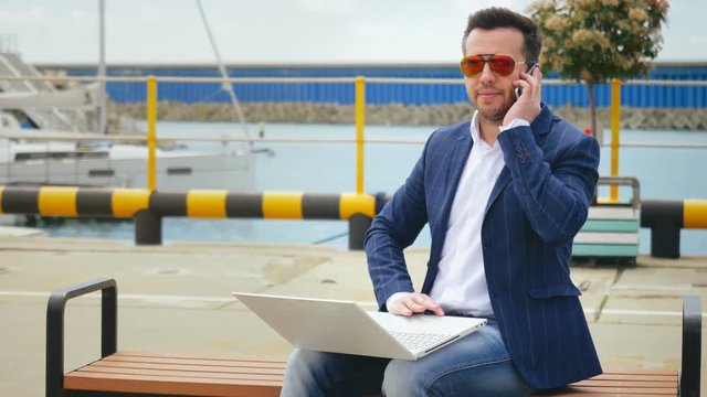 Business man calling by mobile phone and working on portable computer outdoor