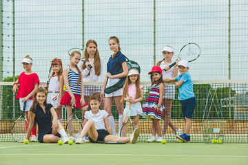 Portrait of group of girls as tennis players holding tennis racket against green grass of outdoor court