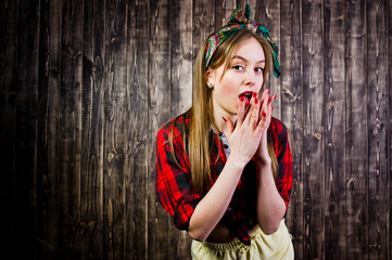 Young funny housewife in checkered shirt and yellow shorts pin up style on wooden background.