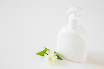 Fototapeta na wymiar White bottle of natural herbal cream for women on gray table. Beautiful jasmine blossoms. Fresh flowers. Care about clean and soft face, hands, legs and body skin. Empty place for text or logo.