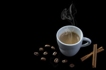 White steamy cup near cinnamon sticks in coffee beans, black background
