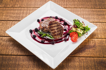 Grilled meat steak with raspberrie sauce on wooden background