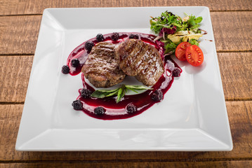 Grilled meat steak with raspberrie sauce on wooden background