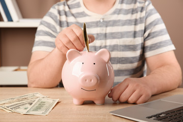 Man putting money into piggy bank on table