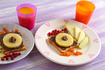 Plates with creative sweet toasts for child and cups of juice on wooden table