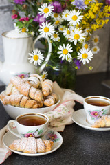 Fototapeta na wymiar Croissants (bagels) with poppy seeds and tea on a bouquet of flowers field background. Morning tea with croissants.